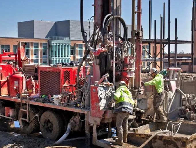Workers with a truck and equipment in a muddy field on North Campus
